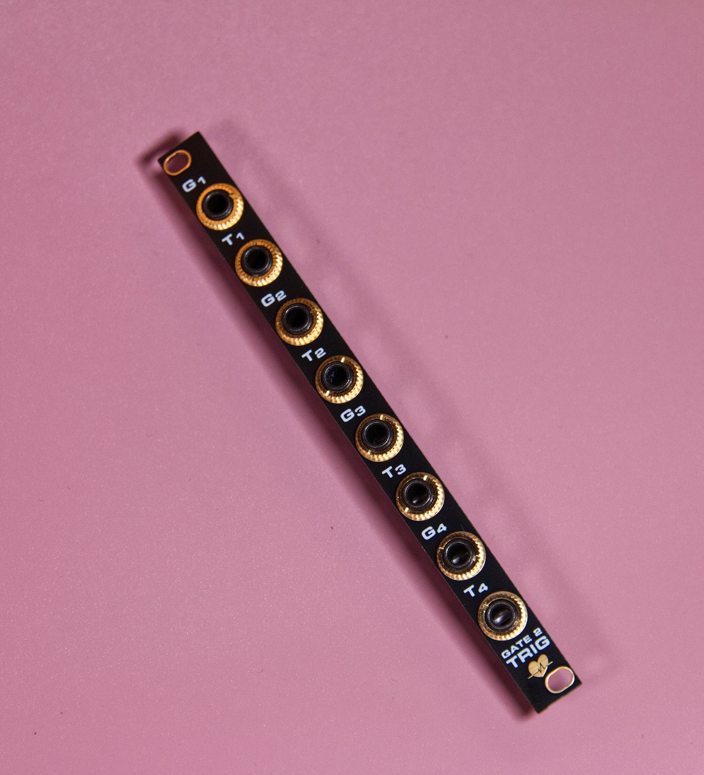 A gate to trigger module for Eurorack rests on a pink mat. It glistens with promise and potential.